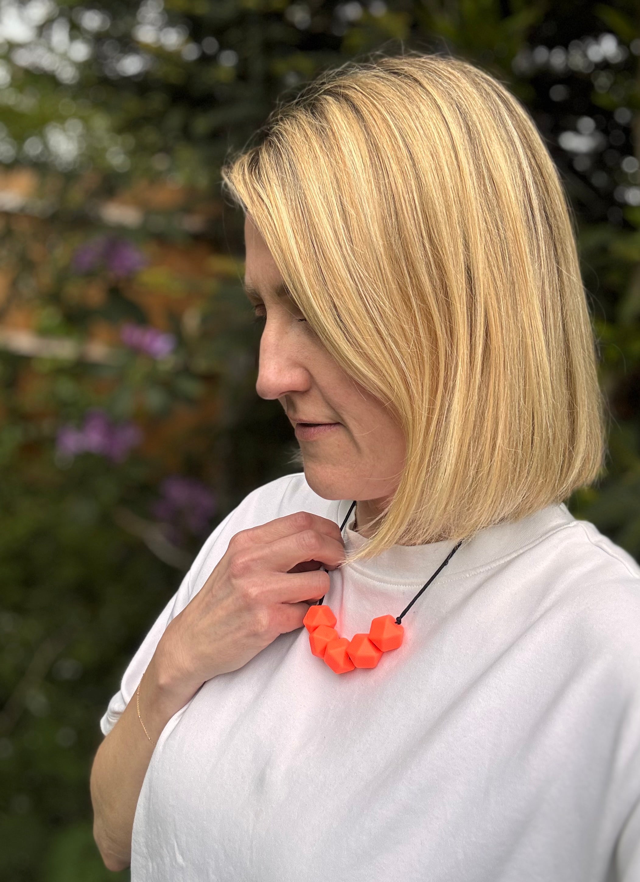 Woman wearing a bright orange necklace outdoors with blurred greenery in the background