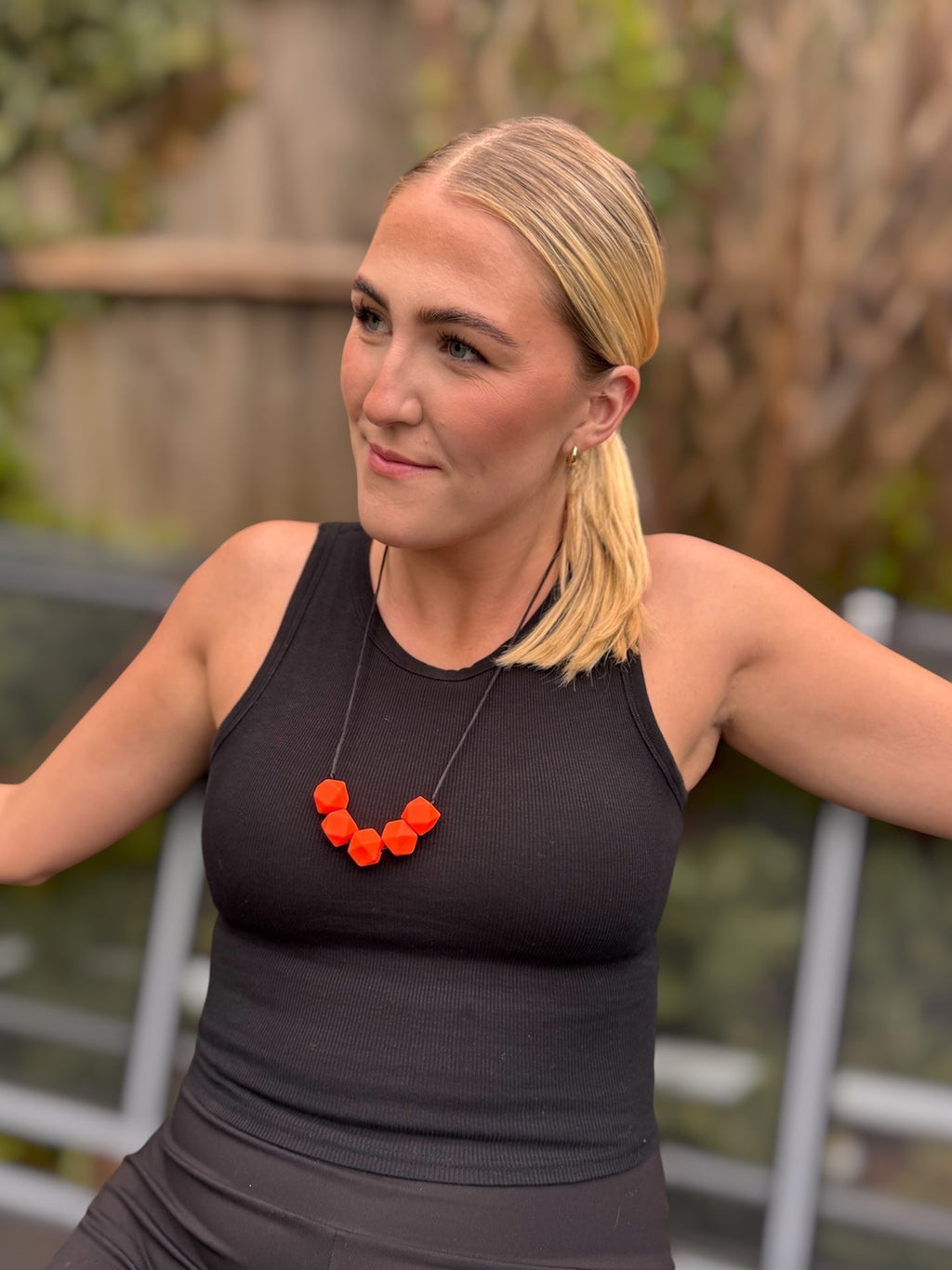 Woman wearing a black top with a neon orange beaded necklace on.